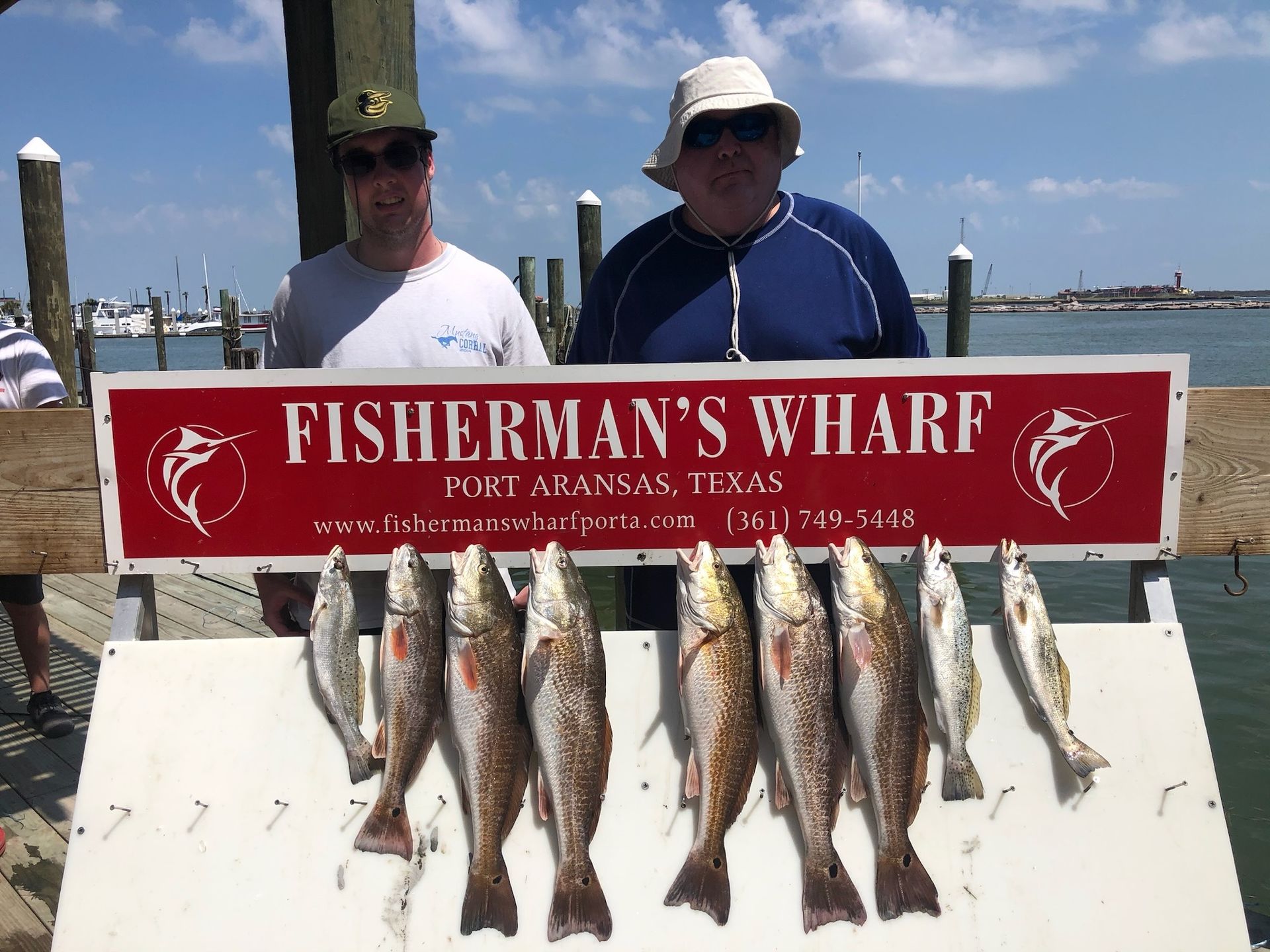 Two men are standing next to a sign that says fisherman 's wharf