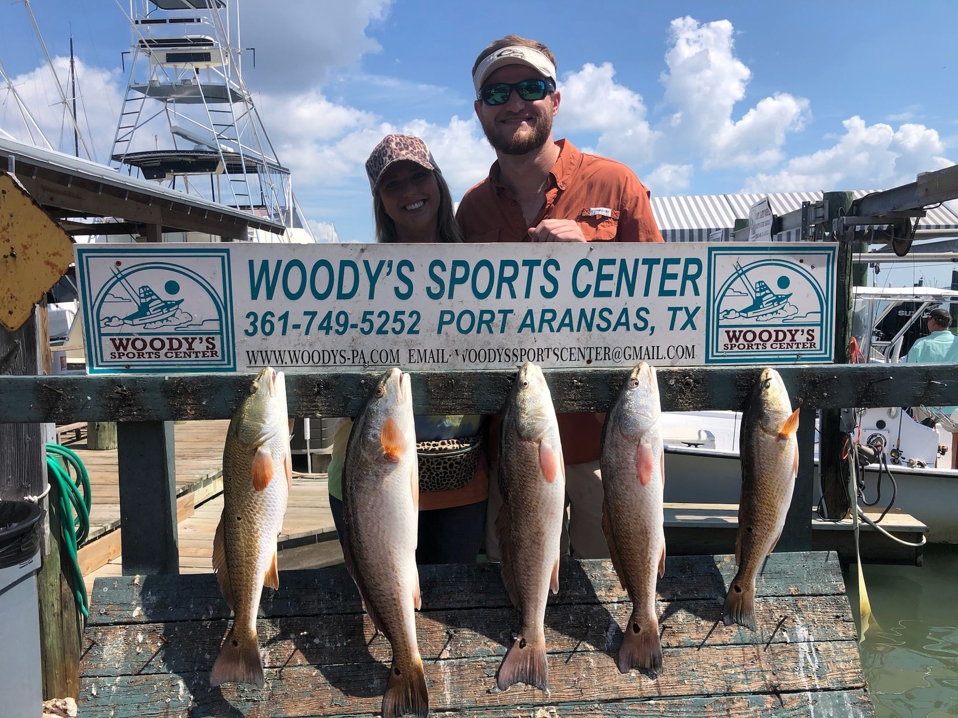 A man and a woman are standing next to a sign that says woody 's sports center.