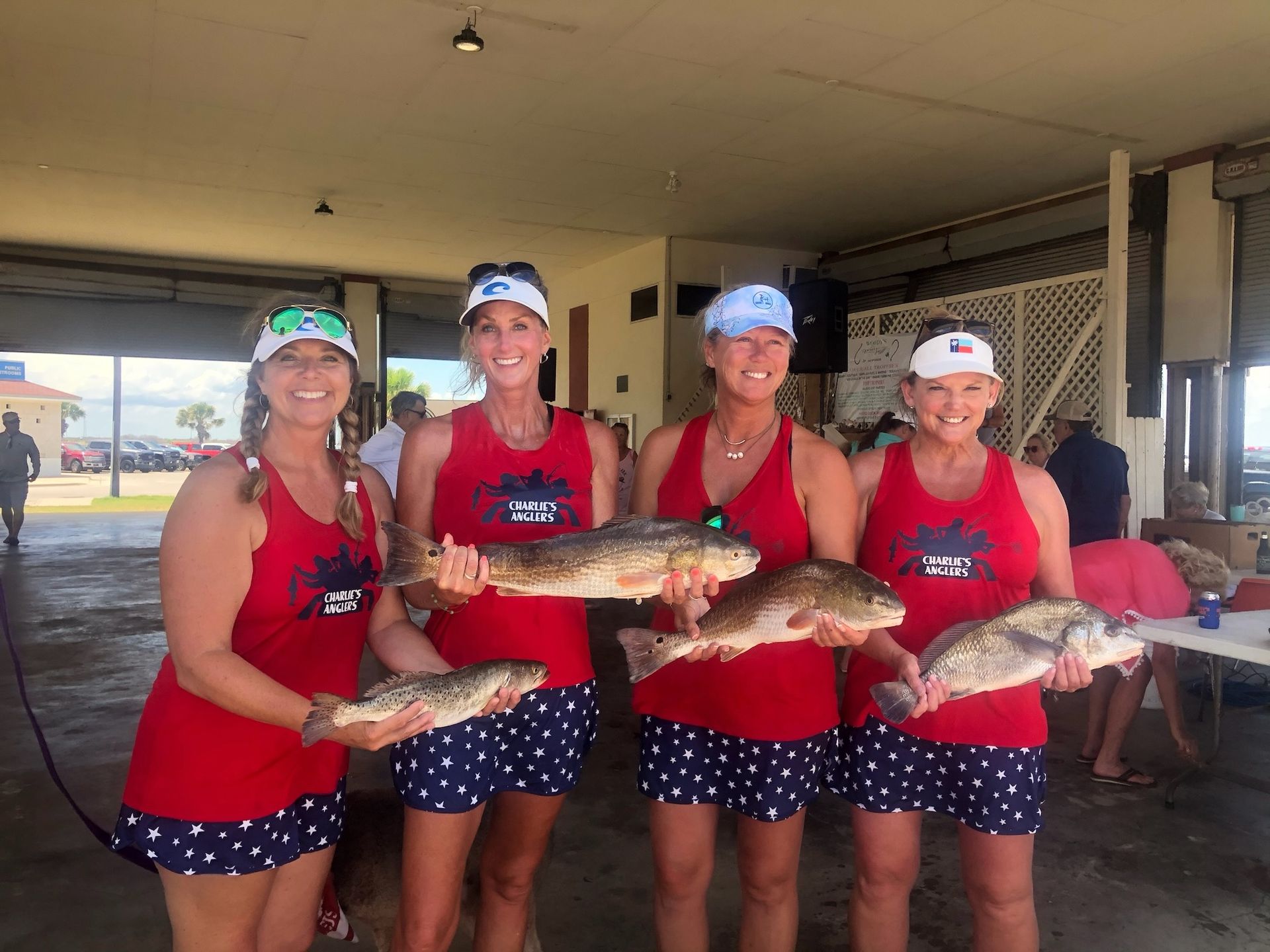 Four women in red tank tops are holding fish in their hands.