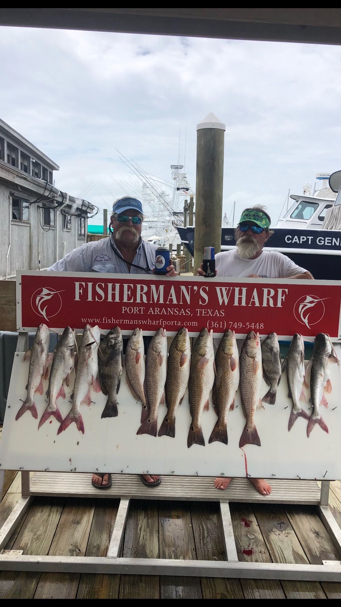 Two men are holding a sign with a bunch of fish on it.