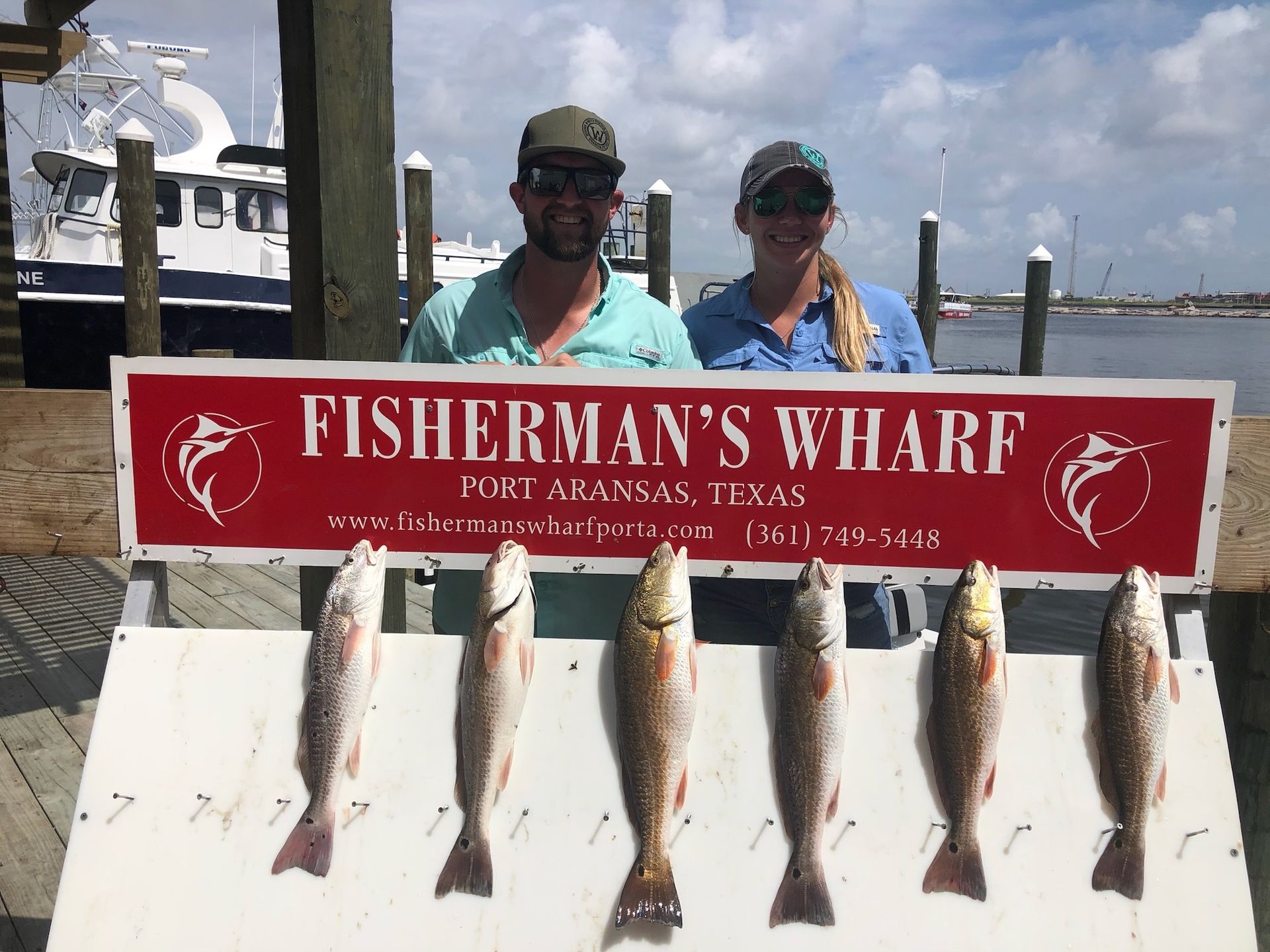 A man and woman standing next to a sign that says fisherman 's wharf