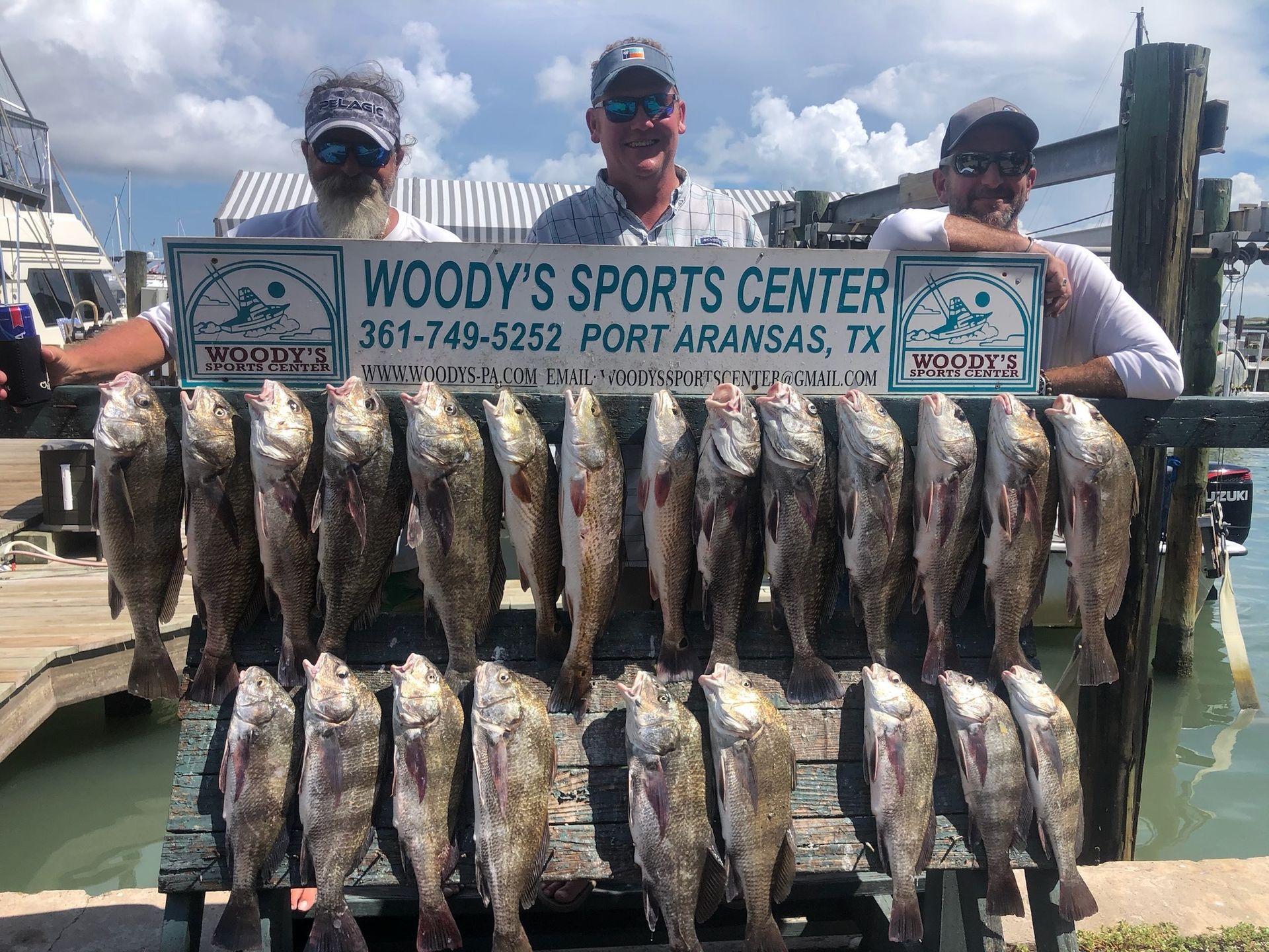 A group of men are standing next to a dock holding a bunch of fish.