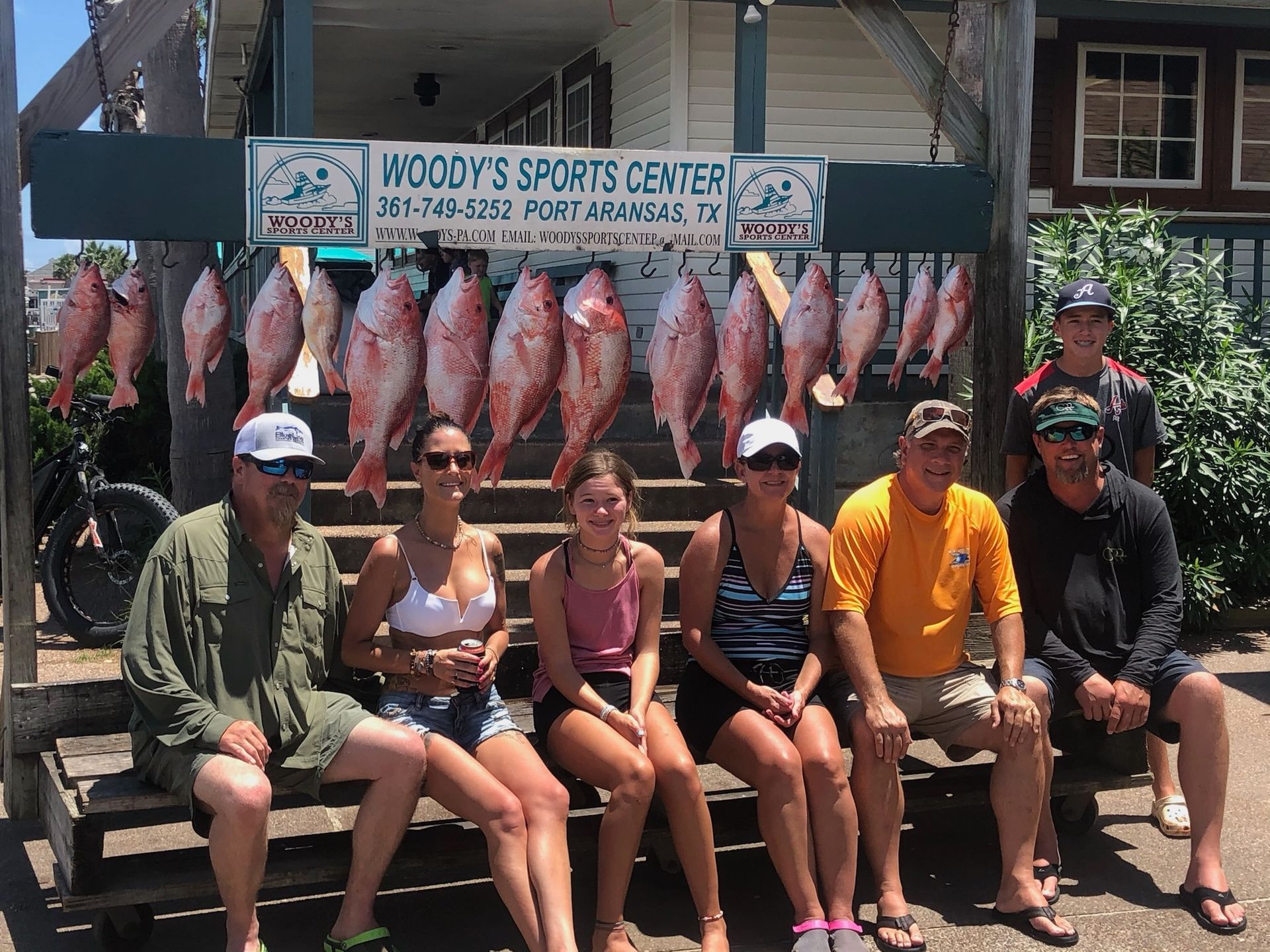 A group of people are sitting on a bench in front of a woody 's sports center sign.