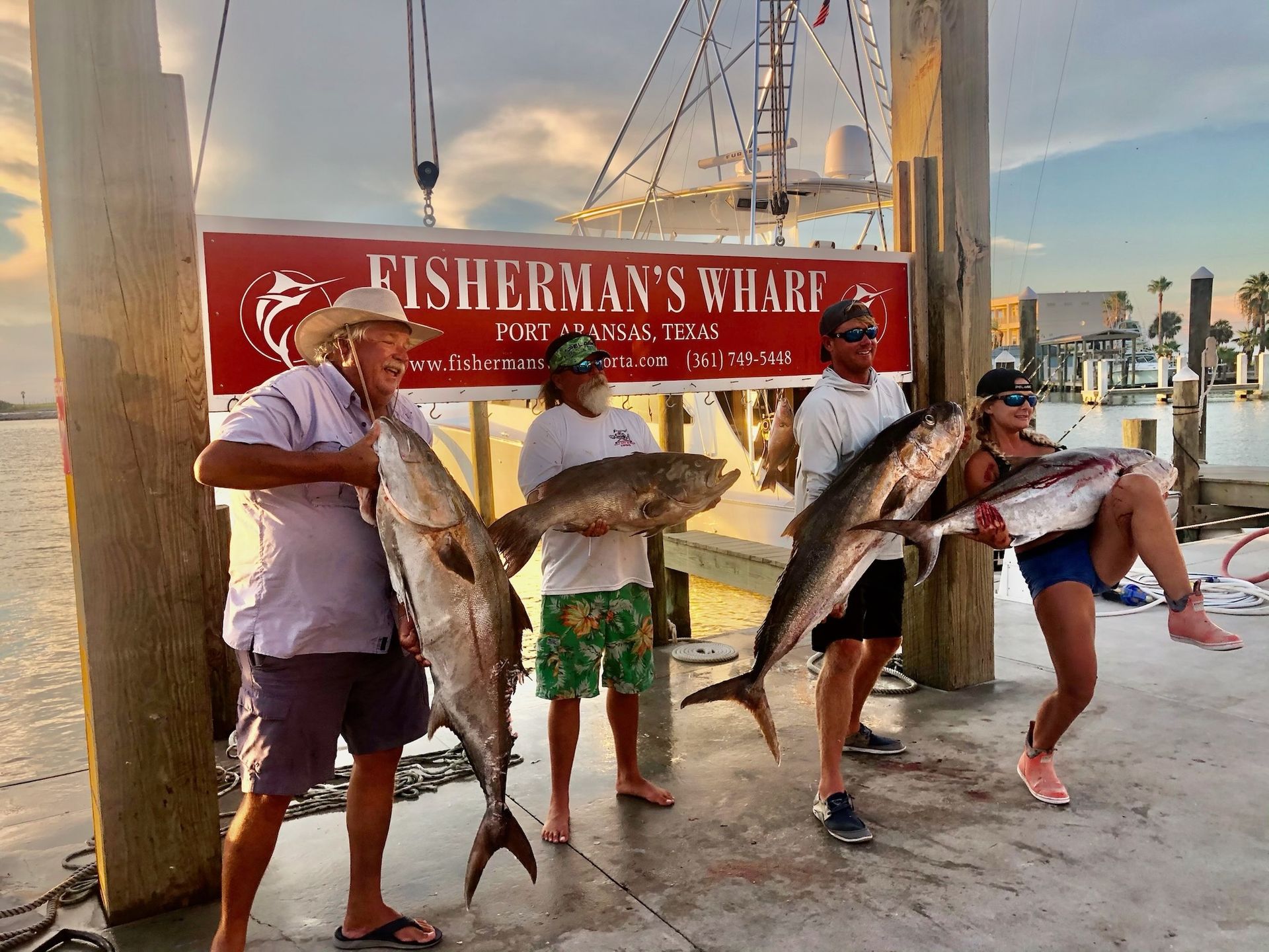 A group of people holding fish in front of a sign that says fisherman 's wharf