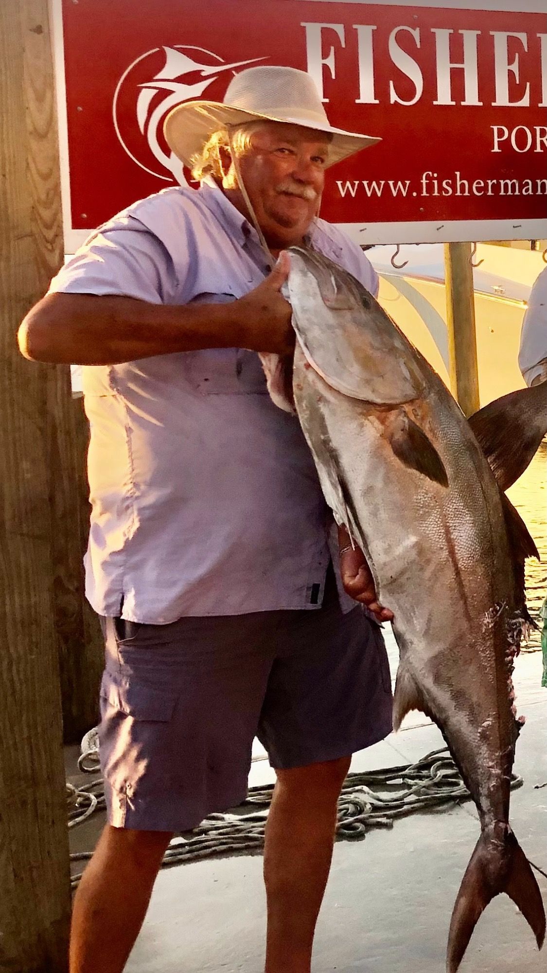 A man is holding a large fish in front of a fisherman 's sign