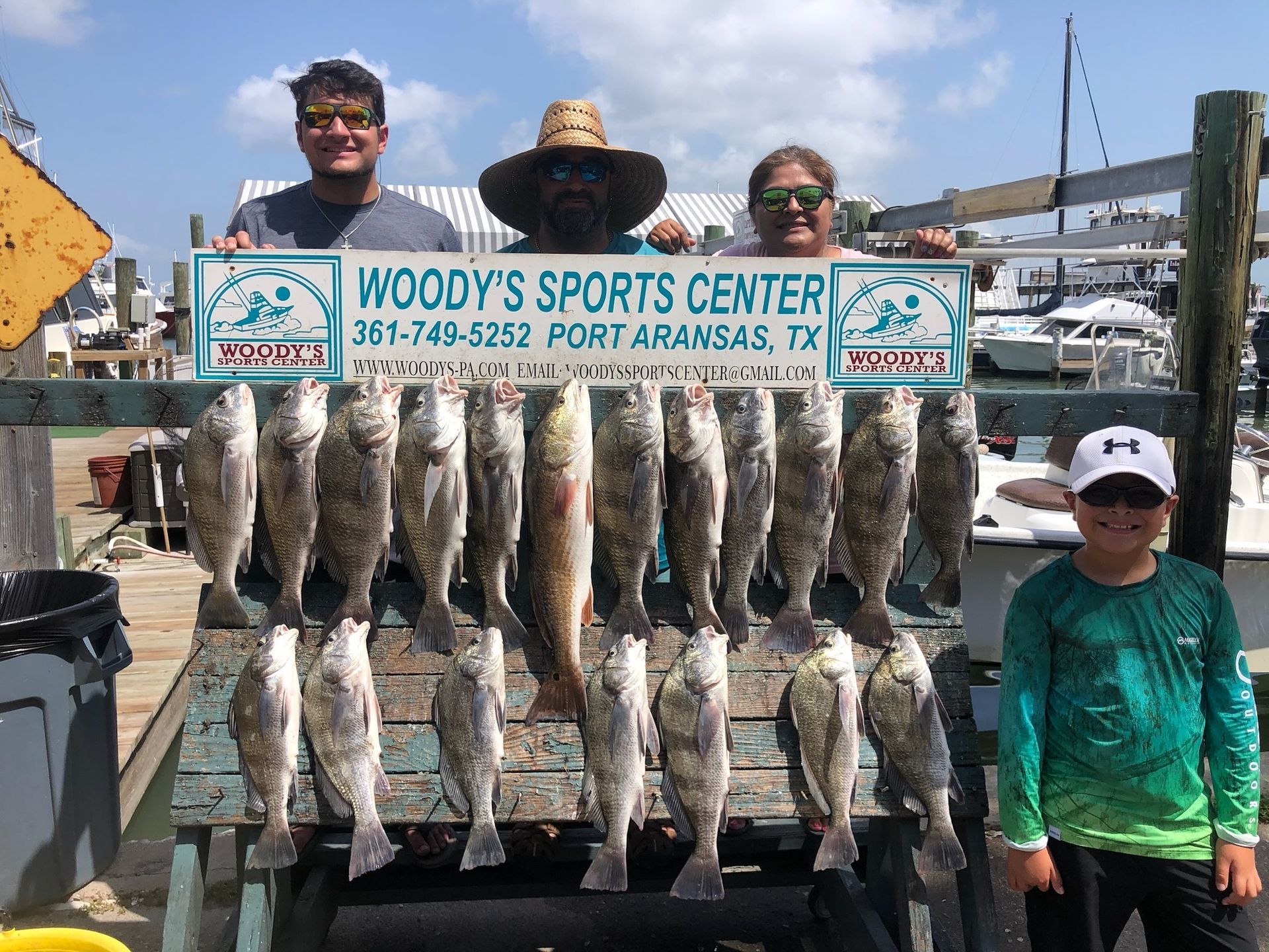 A group of people are standing next to a woody 's sports center sign holding a bunch of fish.