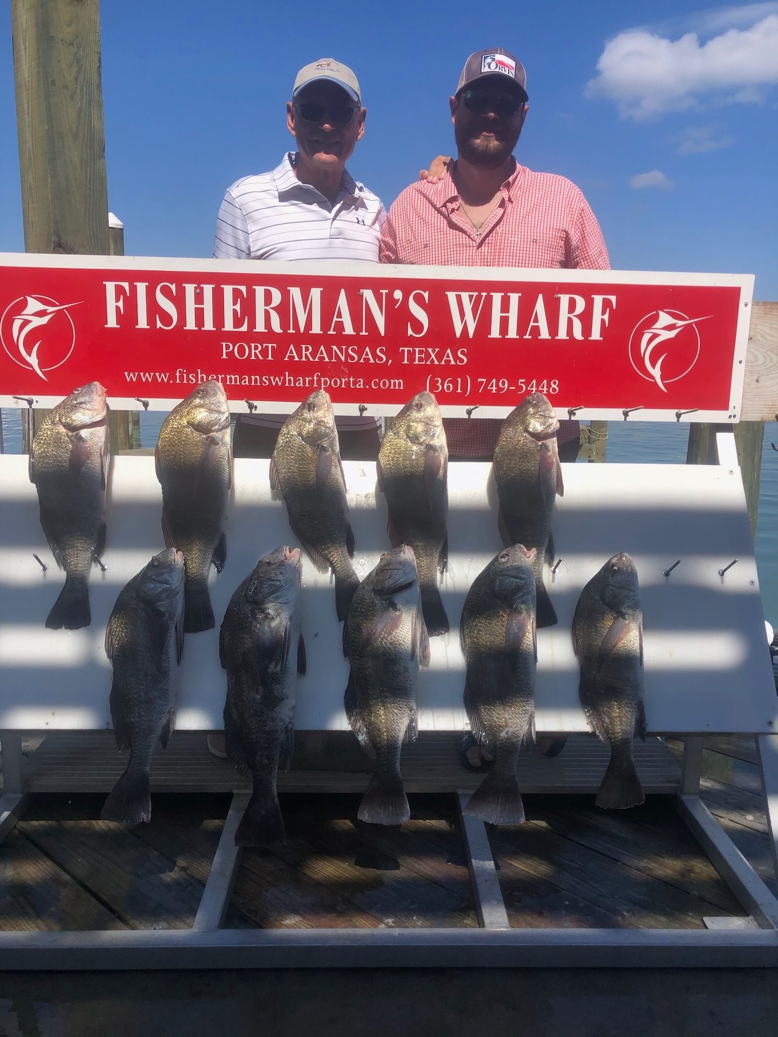 Two men are standing in front of a sign that says fisherman 's wharf.