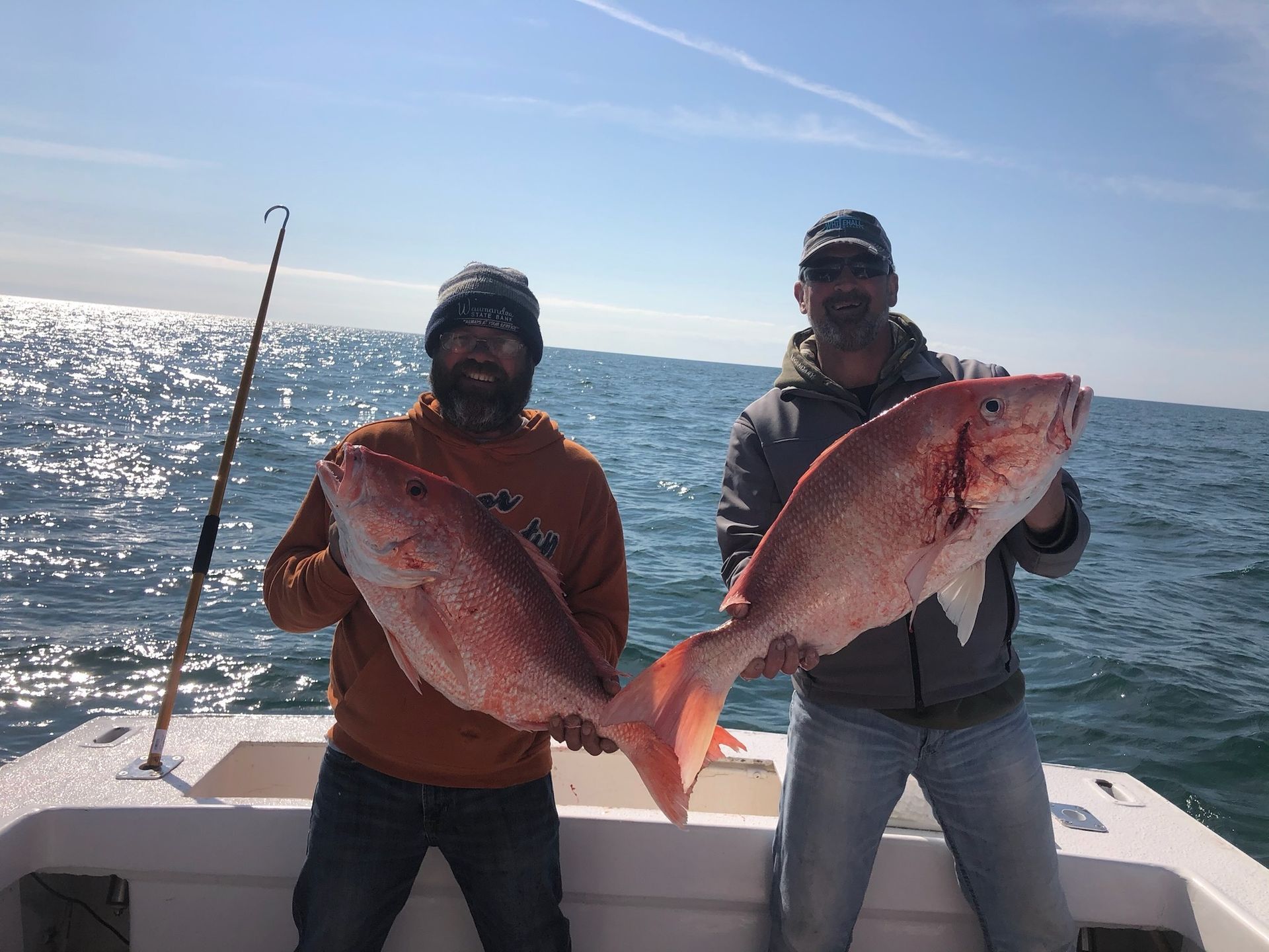 Two men are holding two large red fish on a boat.