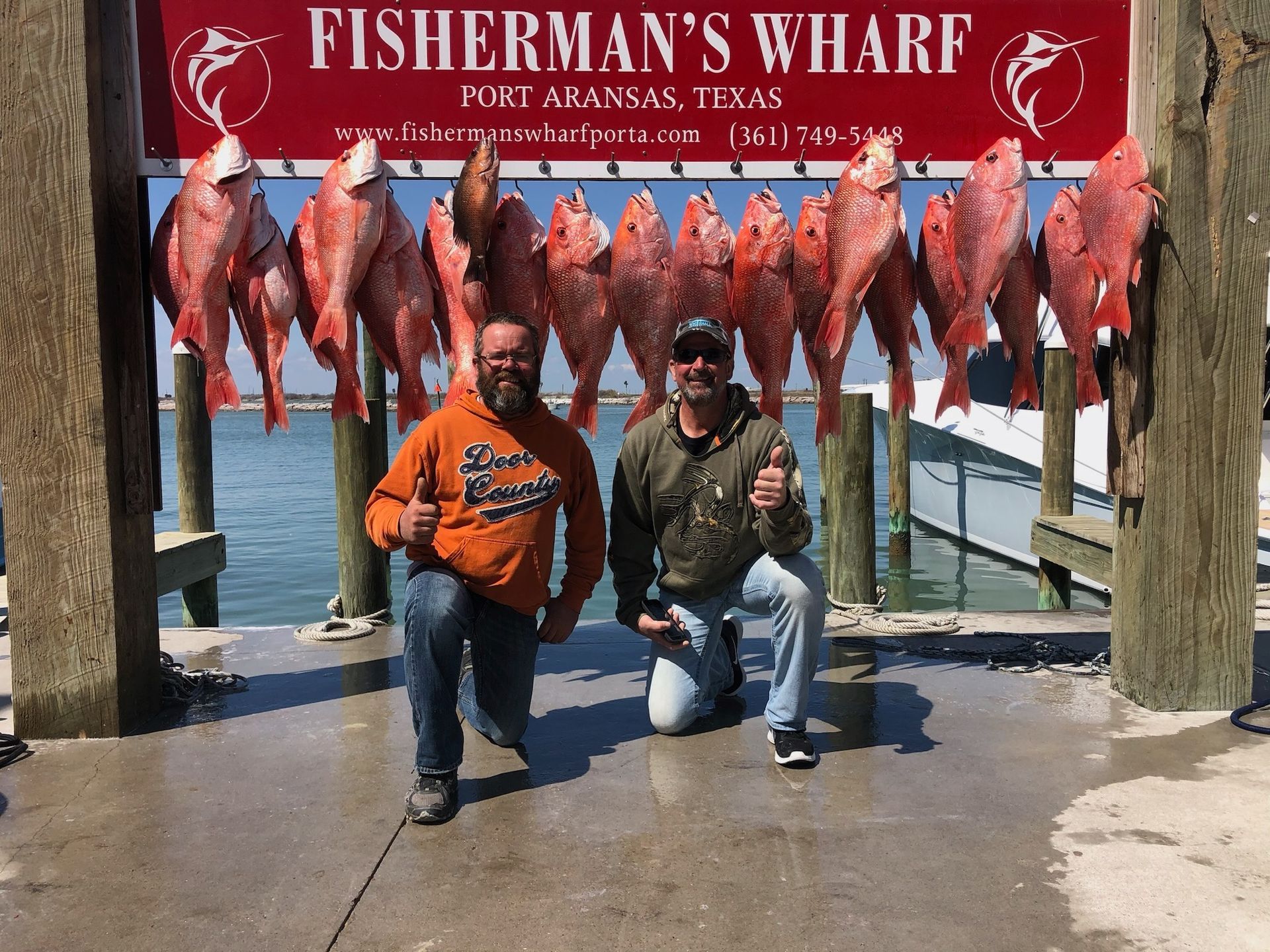 Two men kneeling in front of a sign that says fisherman 's wharf