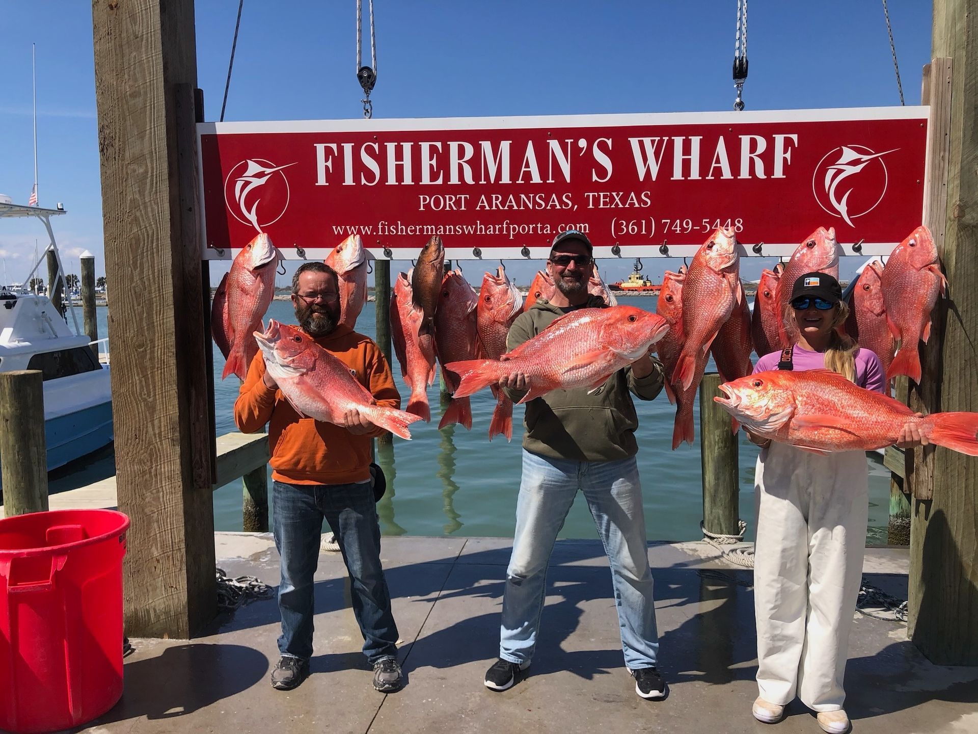 Three men are holding large fish in front of a sign that says fisherman 's wharf.