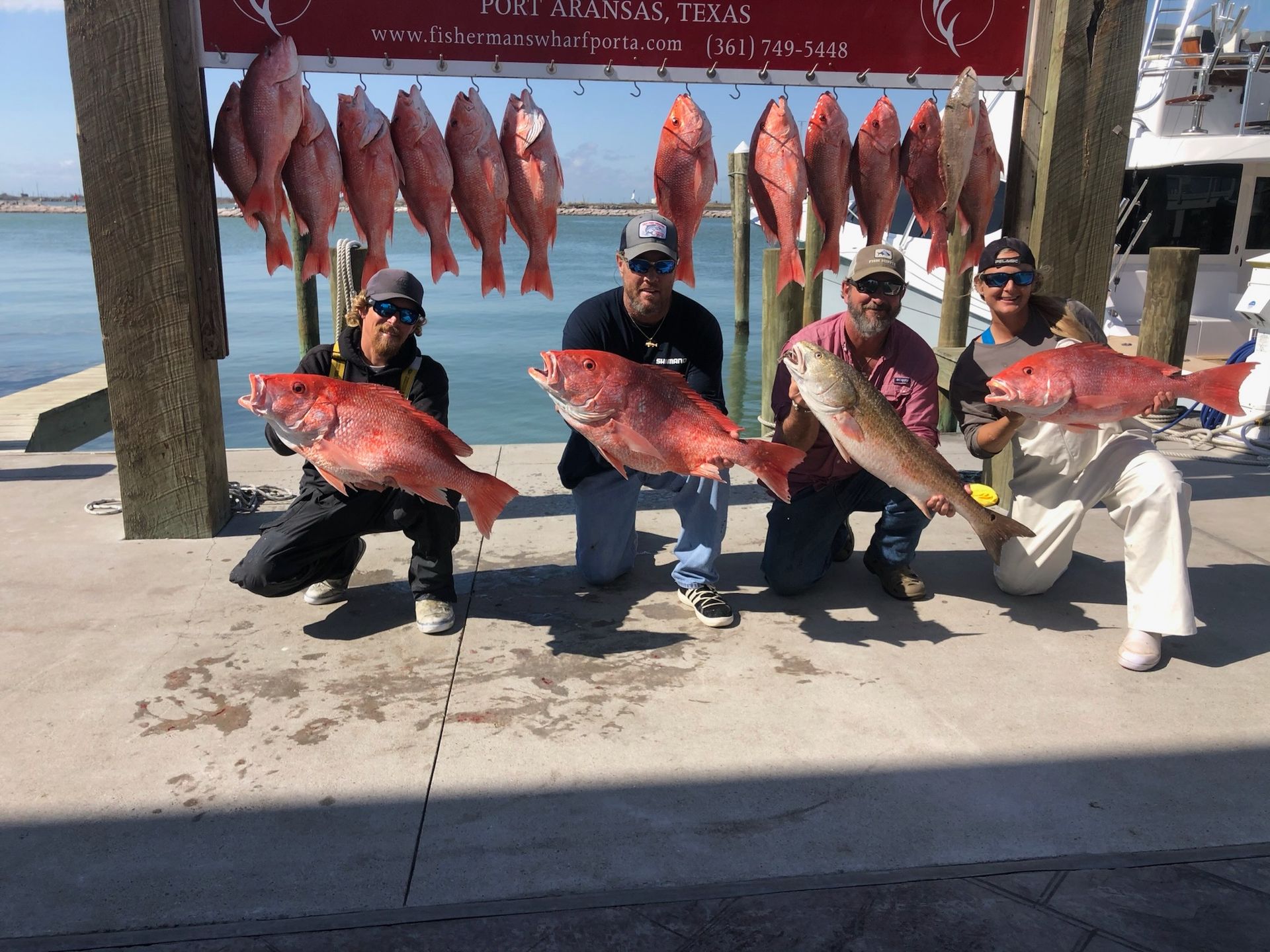 A group of men holding red fish in front of a sign that says texas