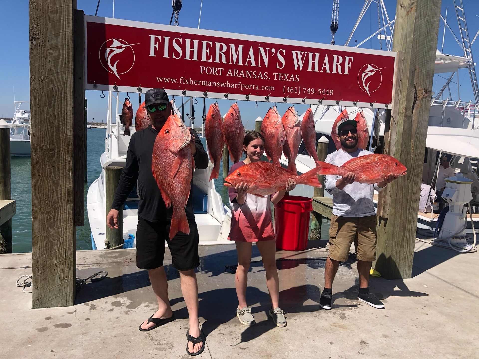 A group of people holding fish in front of a sign that says fisherman 's wharf