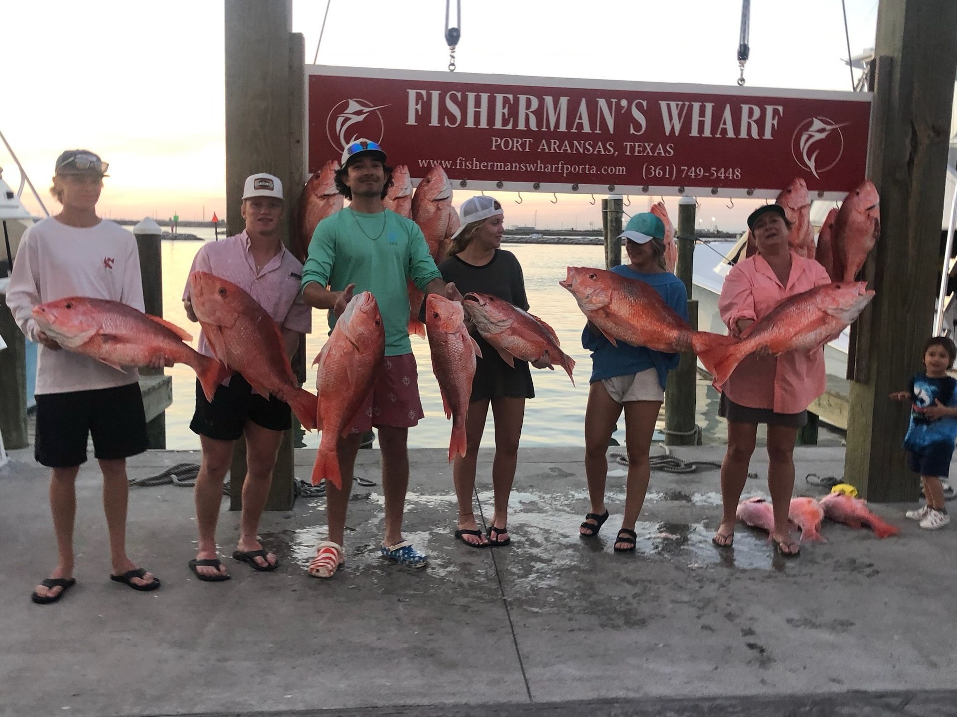 A group of people standing next to each other holding fish in front of a sign that says fisherman 's wharf.