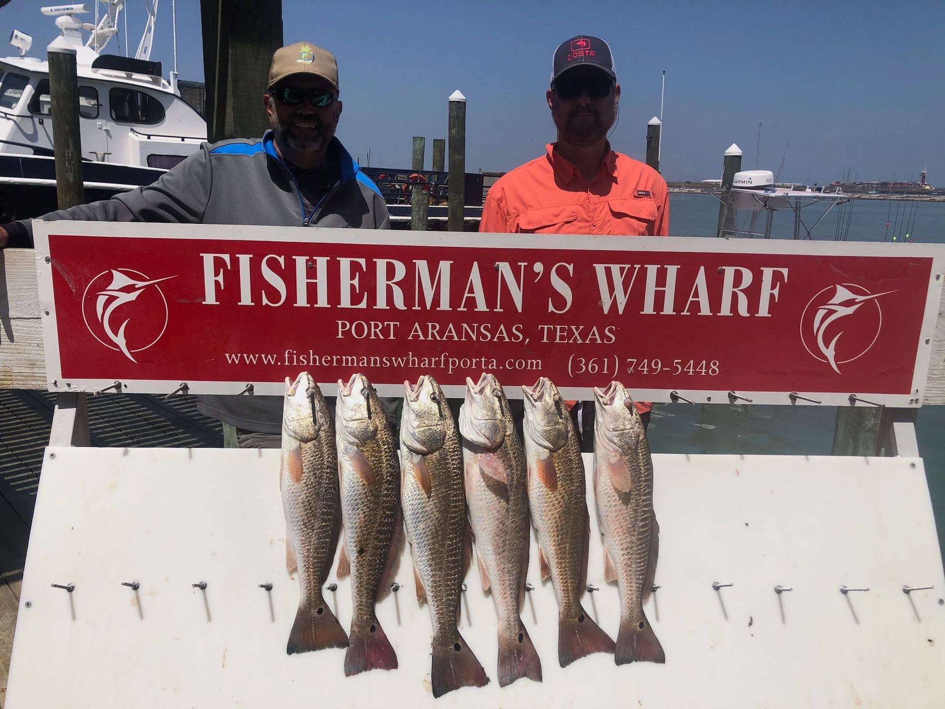Two men are standing next to a sign that says fisherman 's wharf