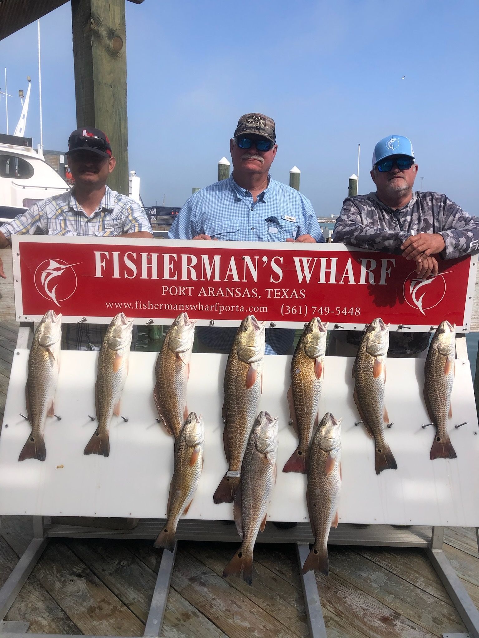 Three men are standing next to a sign that says fisherman 's wharf