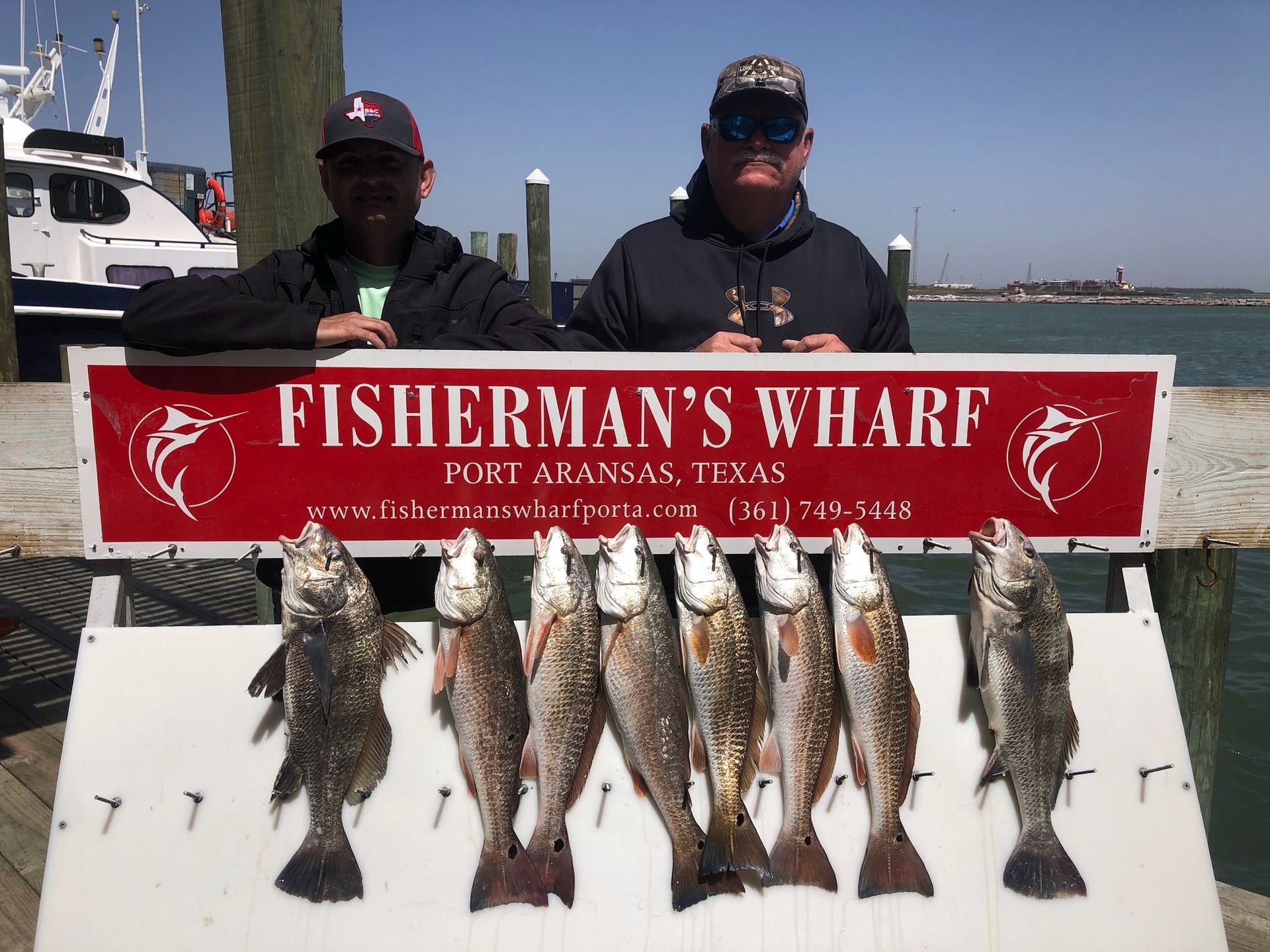 Two men standing next to a sign that says fisherman 's wharf