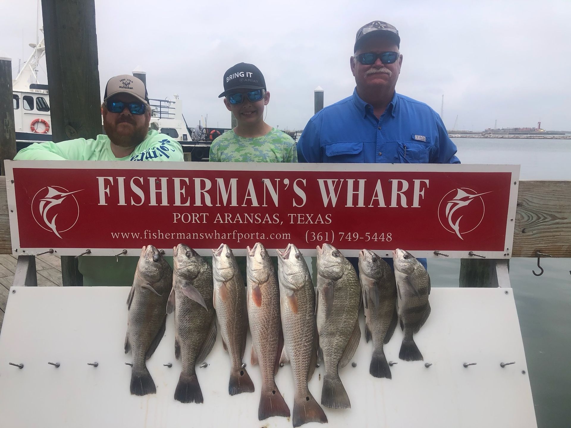 Three men are standing next to a sign that says fisherman 's wharf