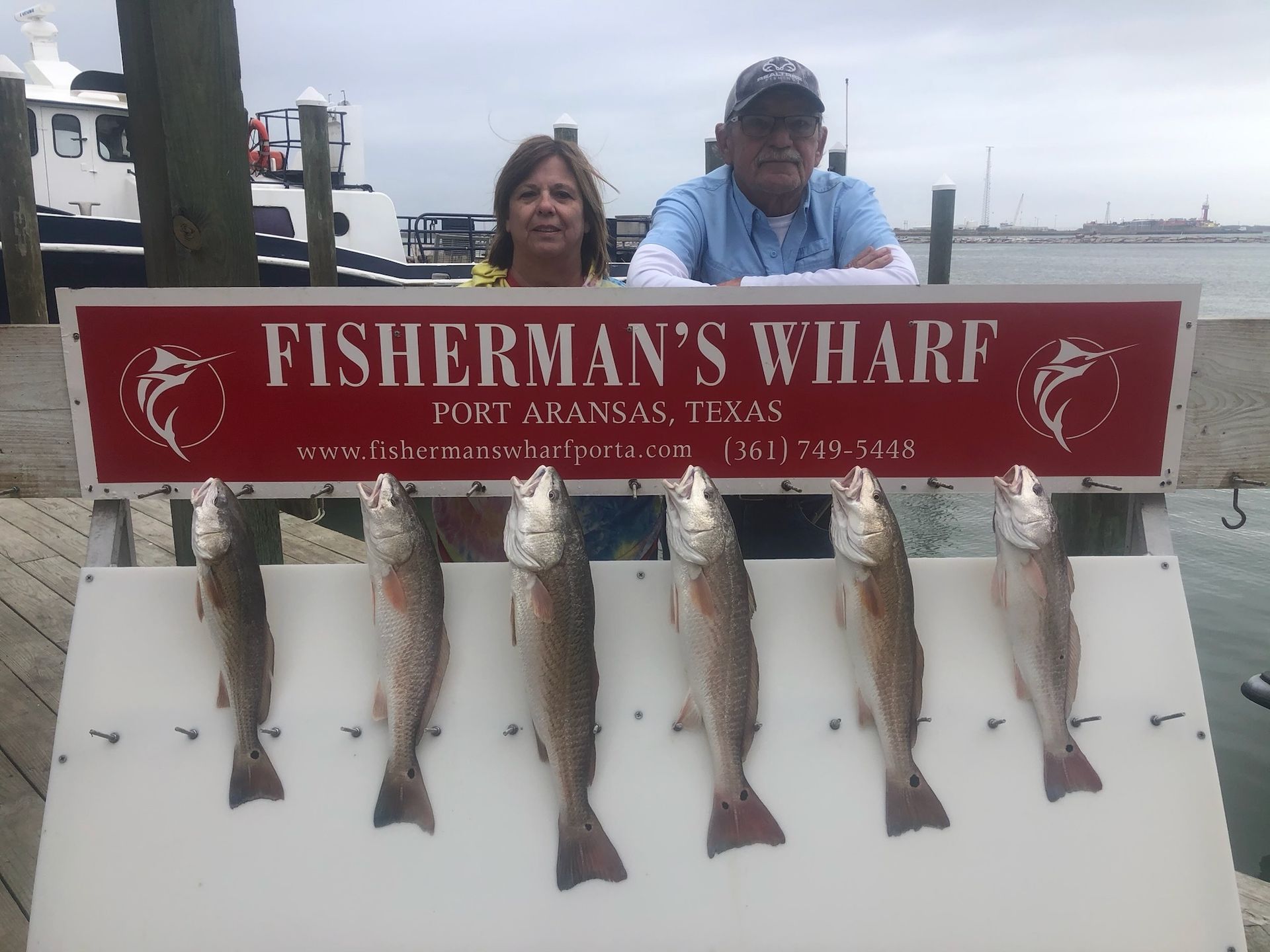 A man and a woman are standing in front of a sign that says fisherman 's wharf.