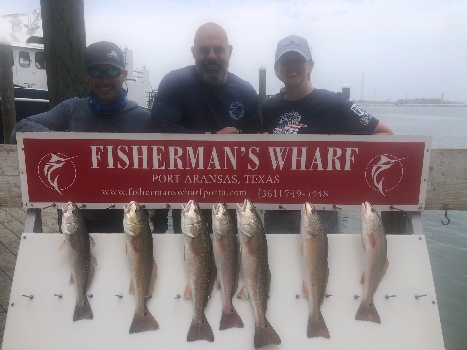 Three men are standing next to a sign that says fisherman 's wharf.