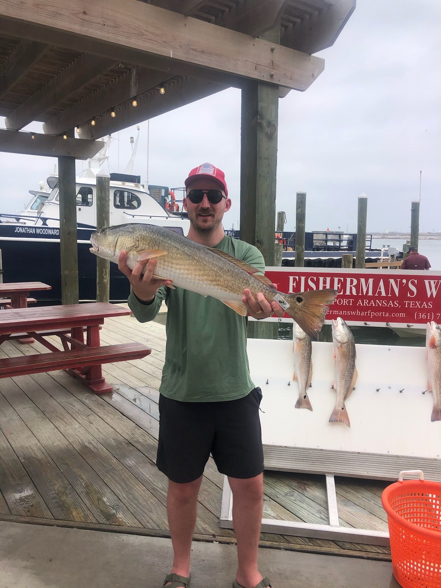 A man is holding a large fish in front of a sign that says fisherman 's w.