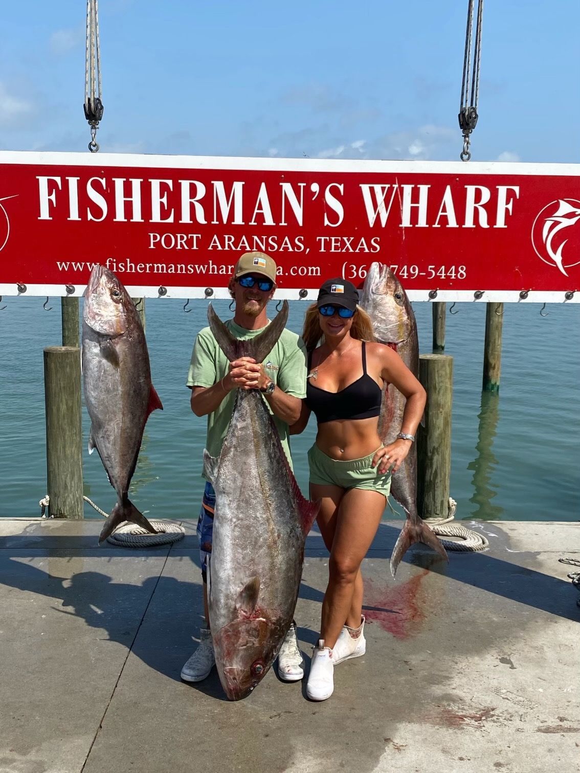 A man and a woman holding a large fish in front of a fisherman 's wharf sign.