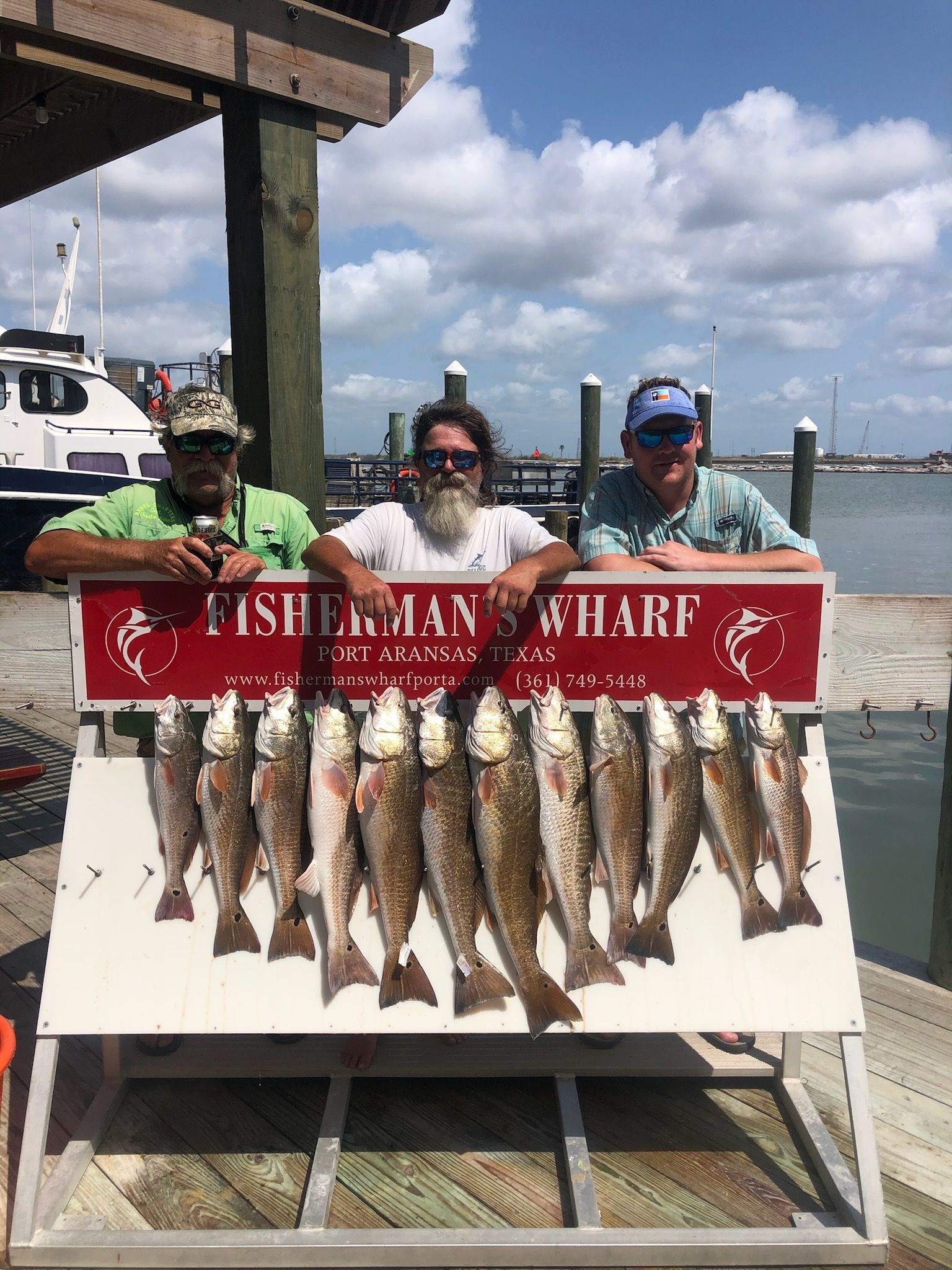 Three men are standing next to a sign holding a bunch of fish.