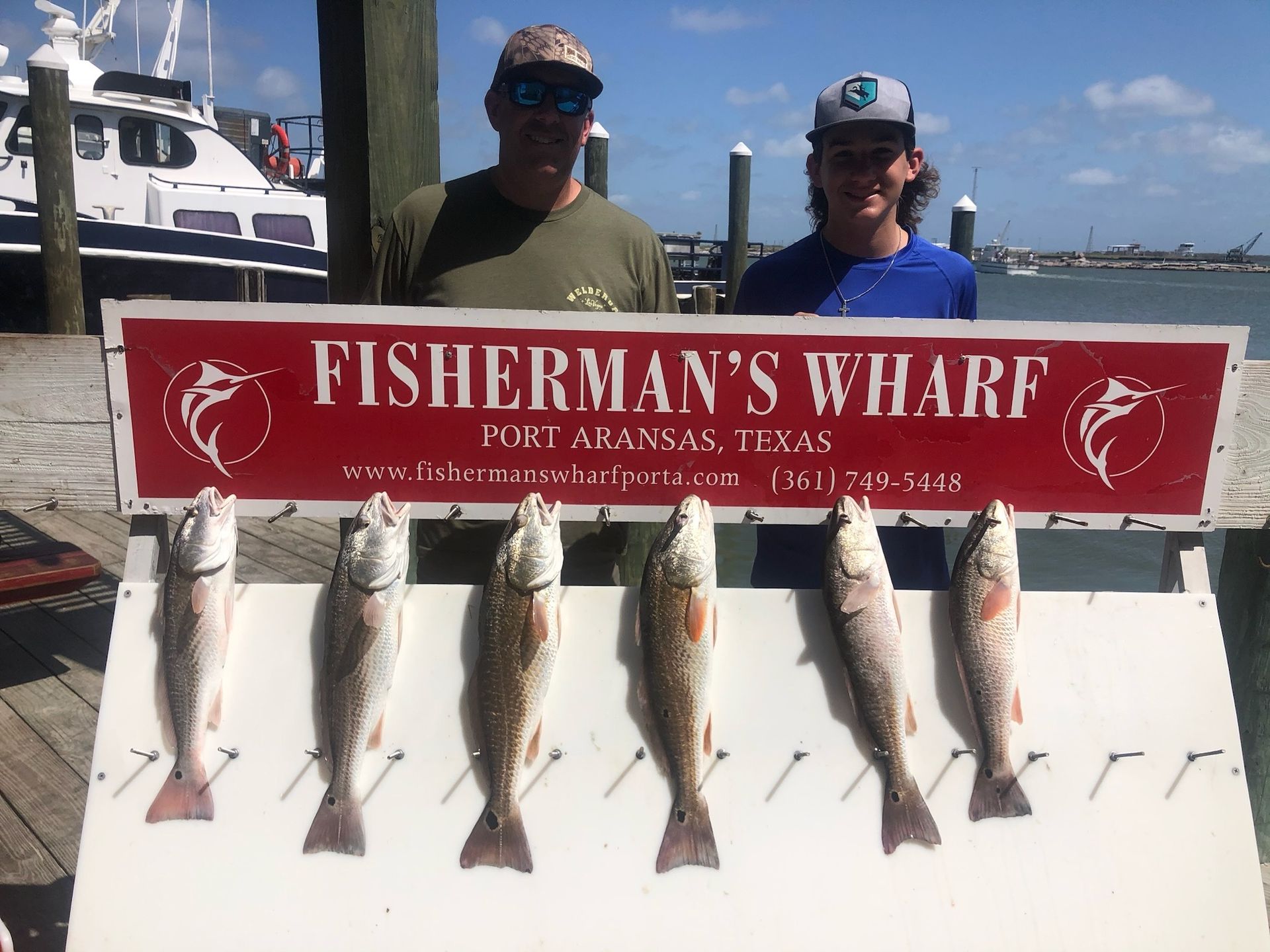 Two men standing next to a sign that says fisherman 's wharf