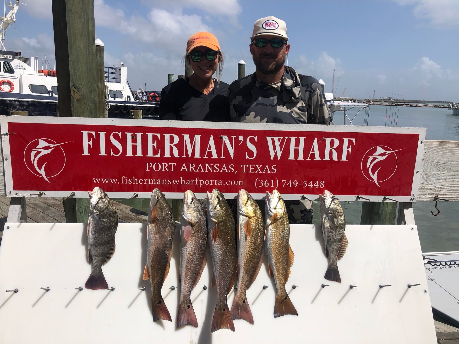Two men are standing next to a sign that says fisherman 's wharf