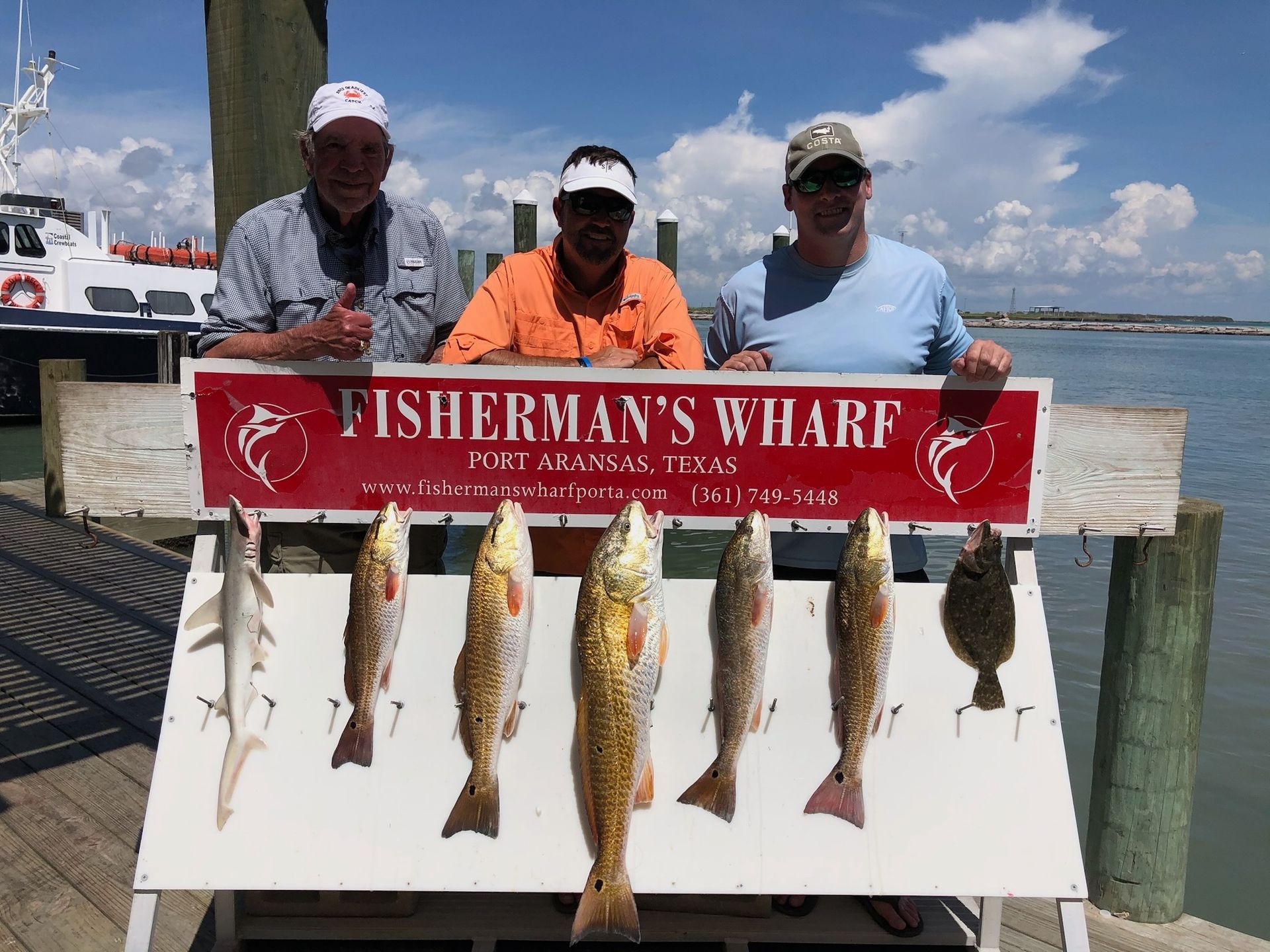Three people are standing next to a sign that says fisherman 's wharf.