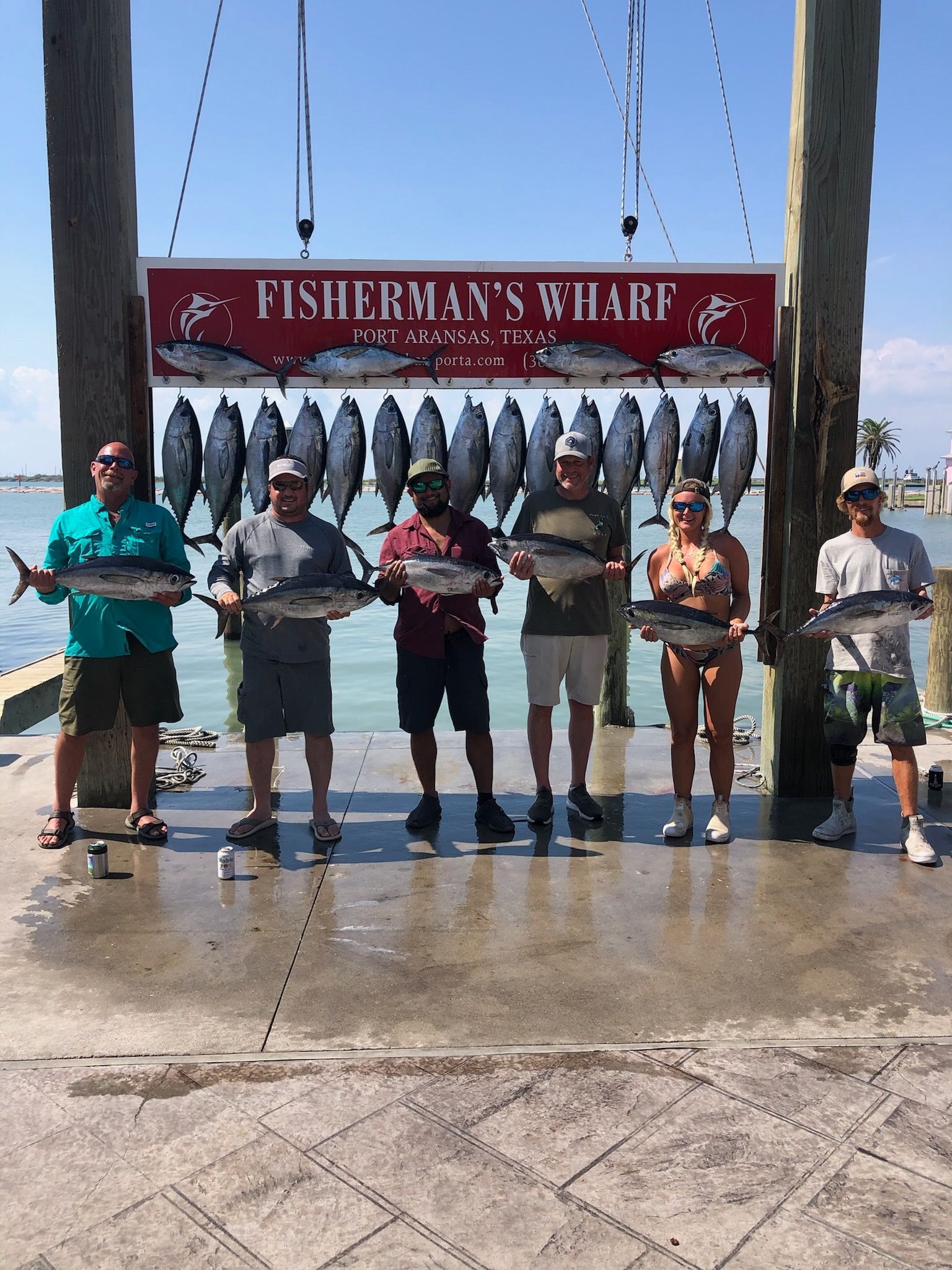 A group of people standing next to each other holding fish in front of a sign that says fisherman 's wharf.