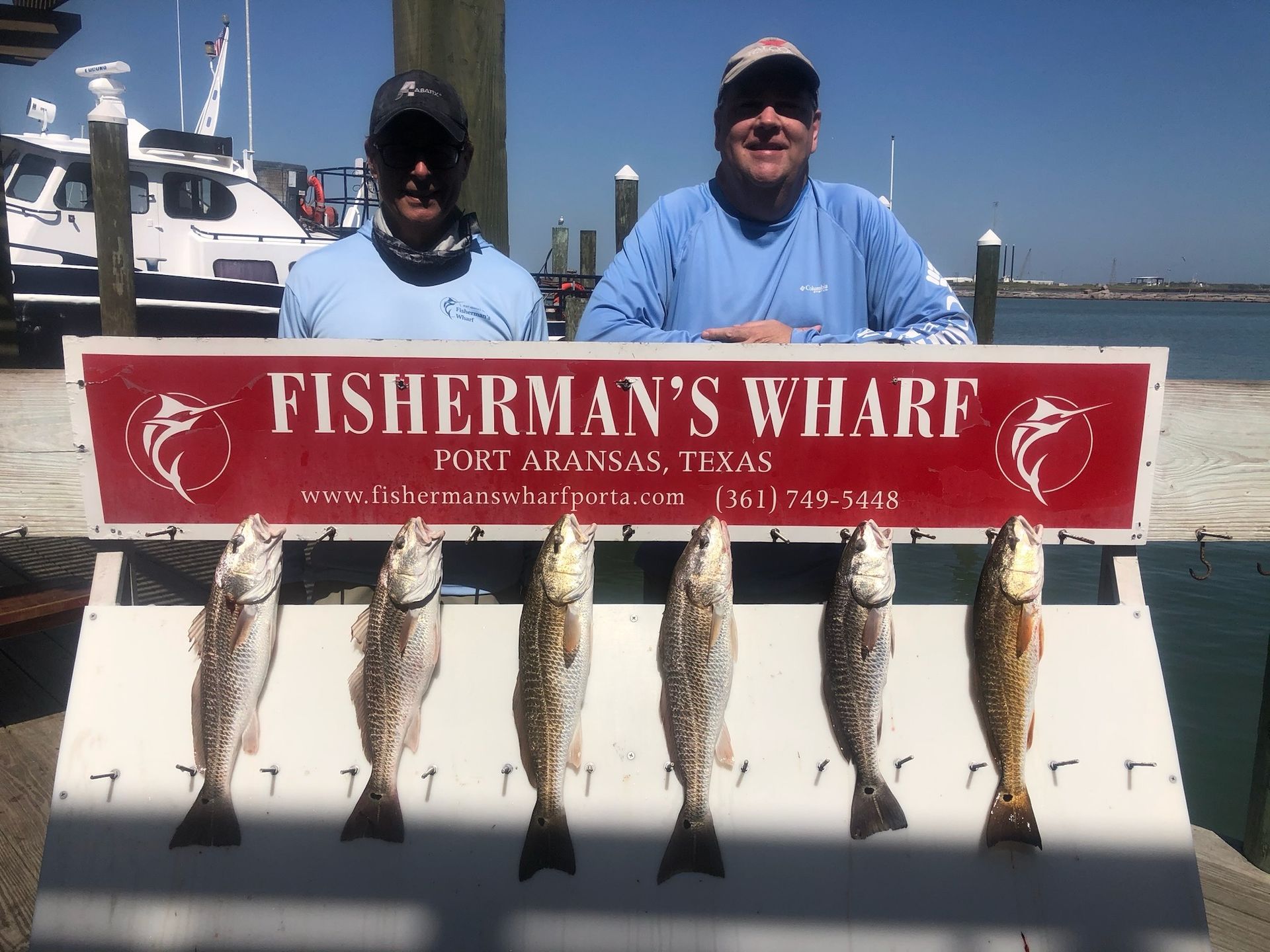Two men are standing next to a sign that says fisherman 's wharf