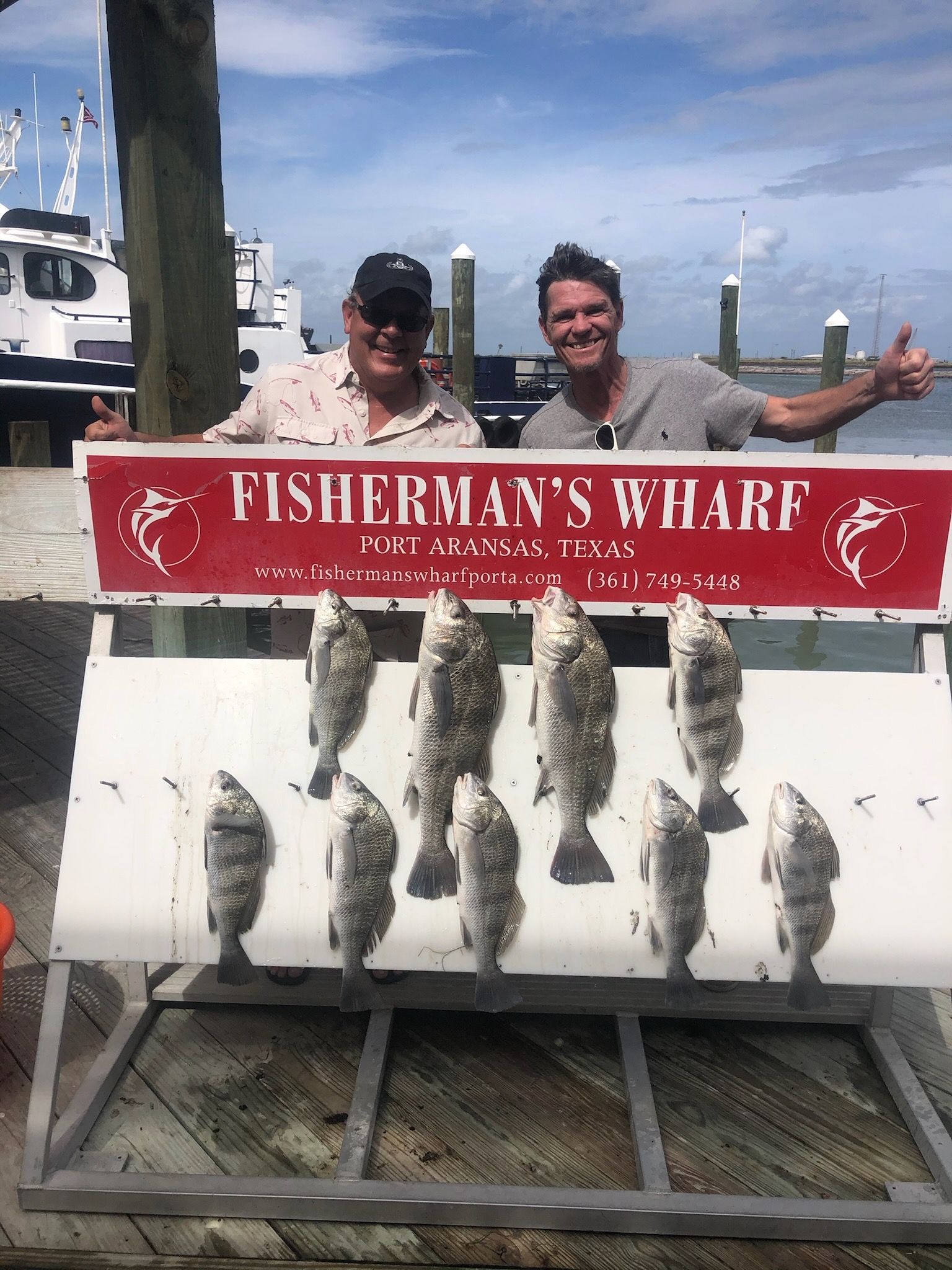 Two men are standing next to a sign that says fisherman 's wharf