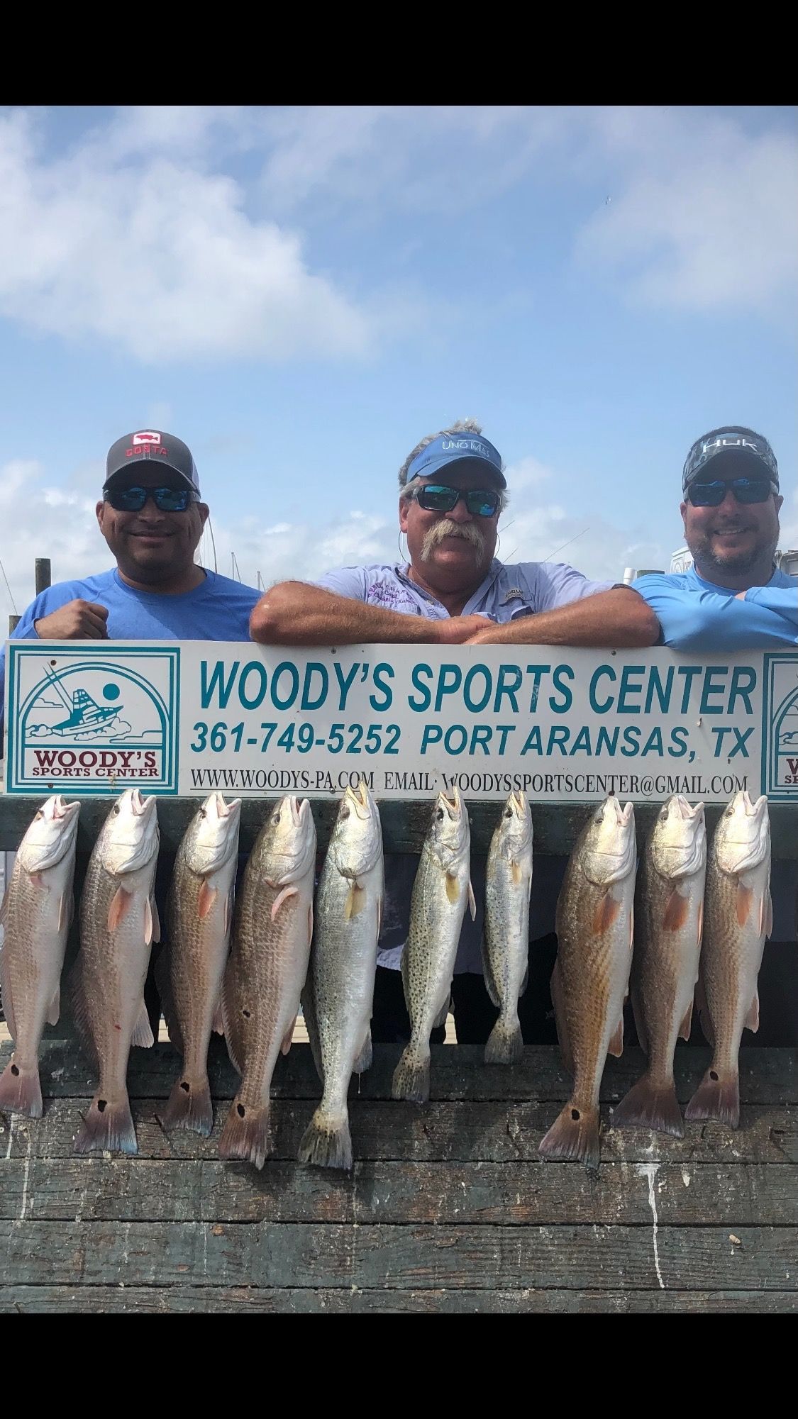 Three men are standing next to a sign holding a bunch of fish.