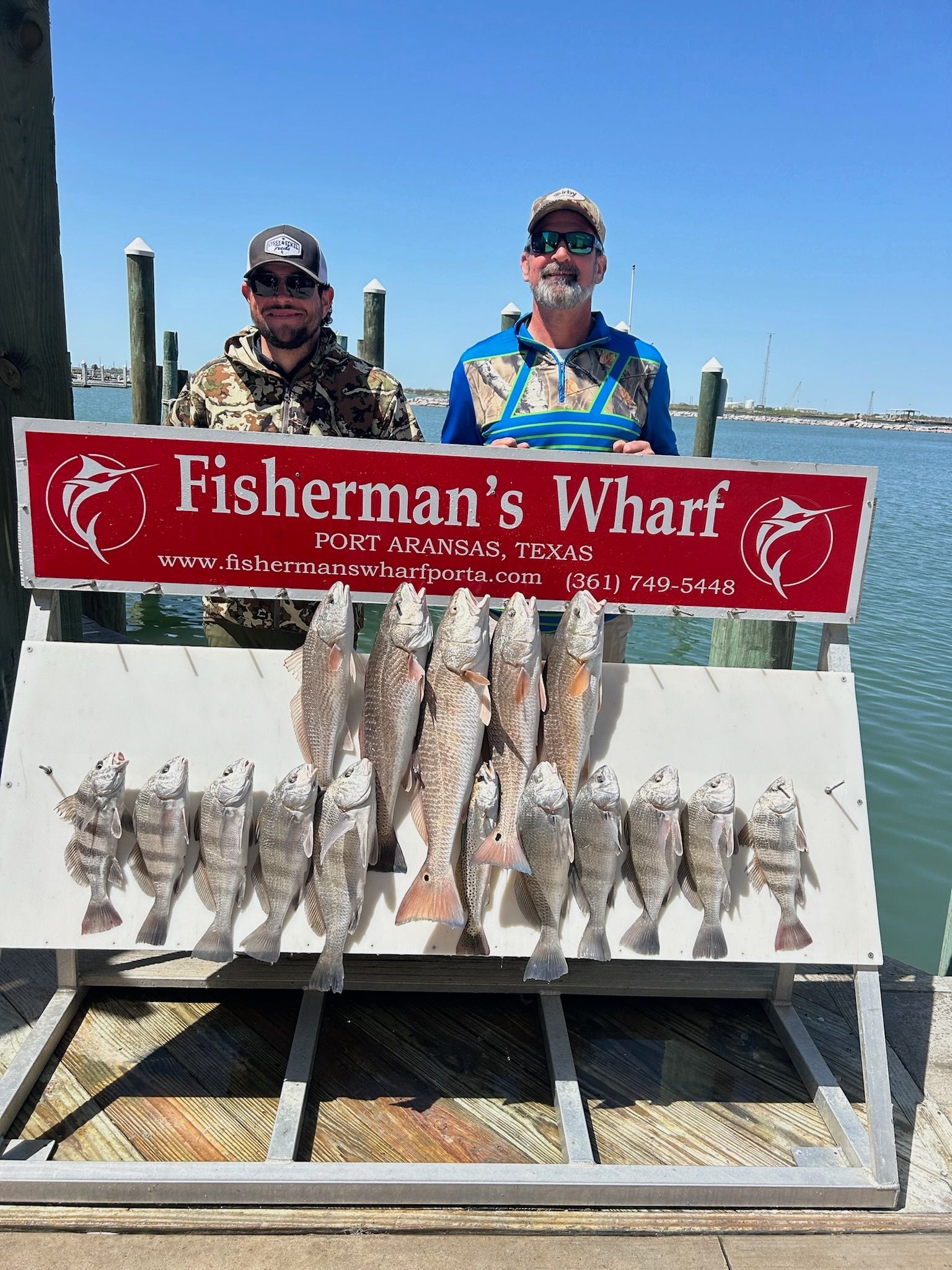 Two men are standing next to a sign that says fisherman 's wharf.