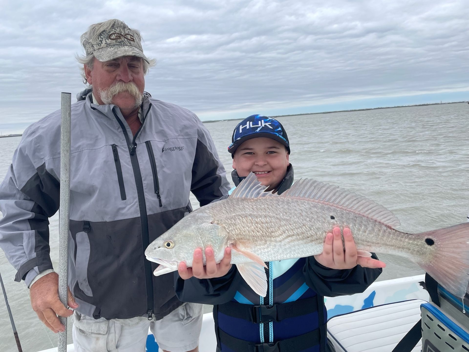 A man and a boy are holding a large fish on a boat.