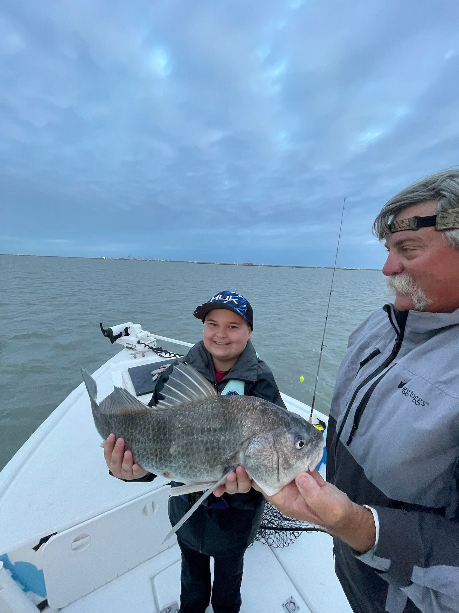 A man and a boy are holding a large fish on a boat.