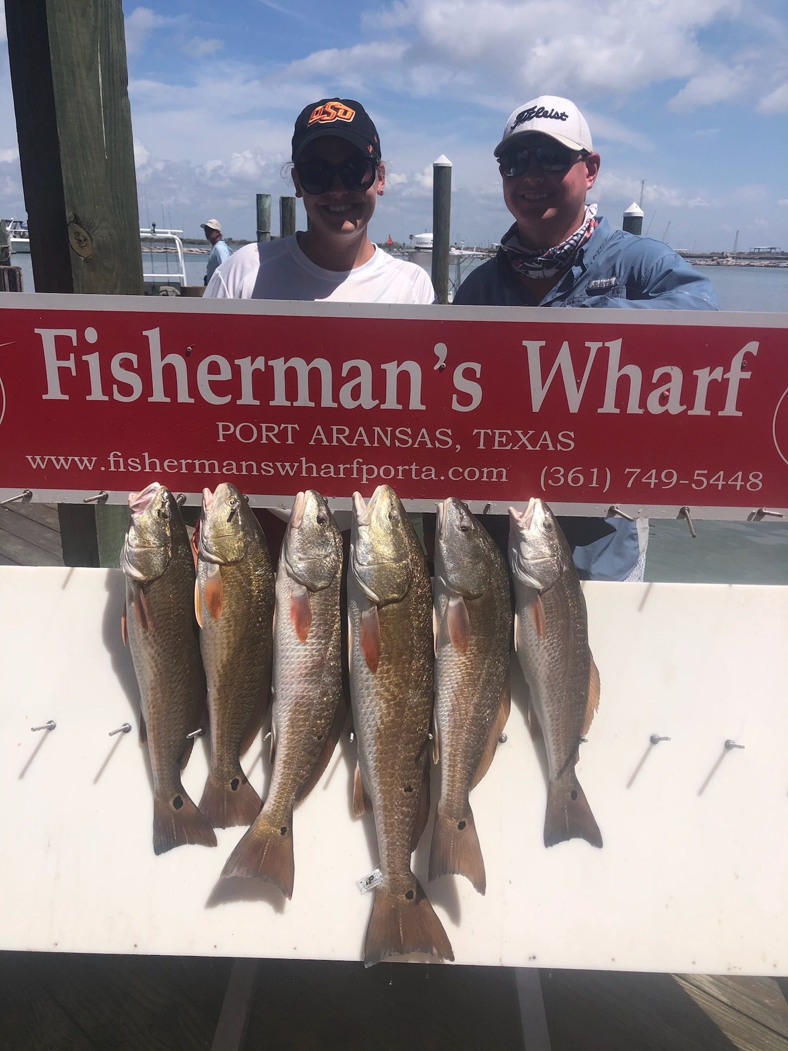 Two men are standing behind a sign that says fisherman 's wharf