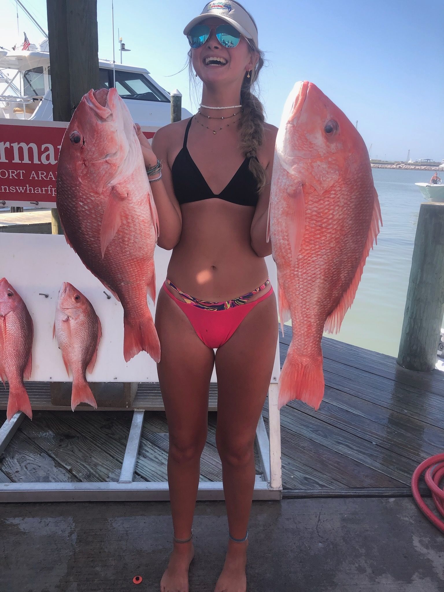 A woman in a bikini is holding two large red fish.