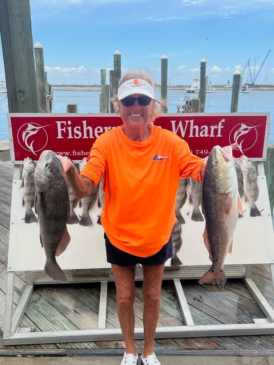 A woman holding a bunch of fish in front of a sign that says fisher wharf