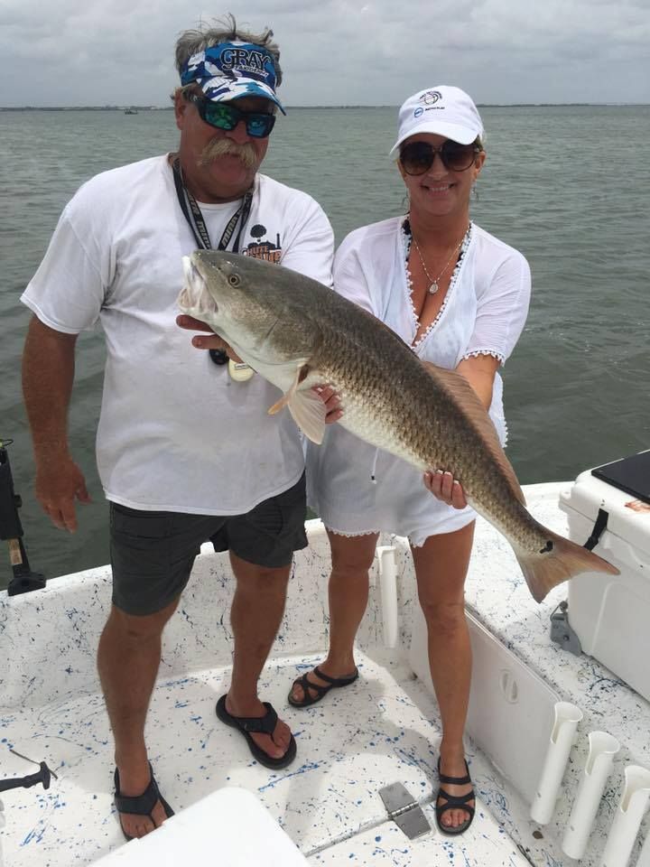 A man and a woman are standing on a boat holding a large fish.