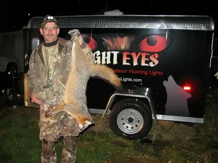 Hunter holding a large fish beside a Night Eyes hunting lights trailer at night