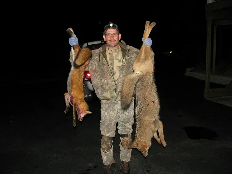 Hunter holding two dead deer by the legs at night, wearing camouflage clothing.