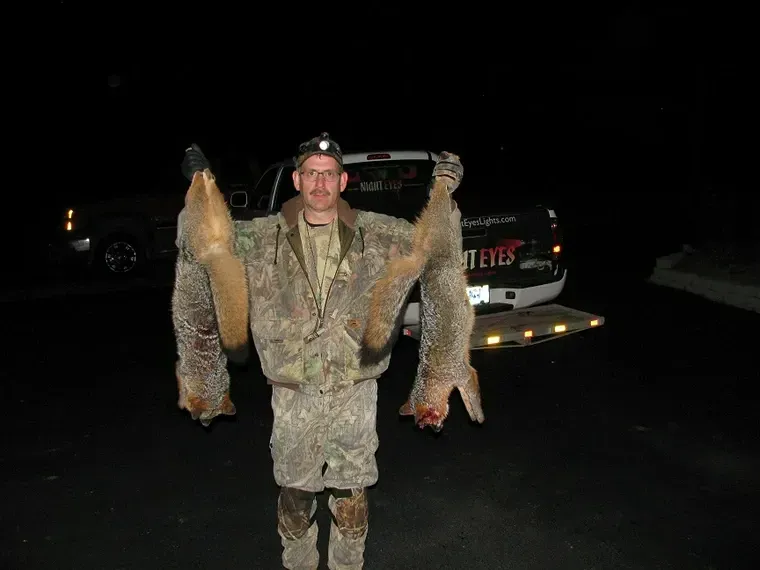 Person in camouflage holding two large fish beside a vehicle at night