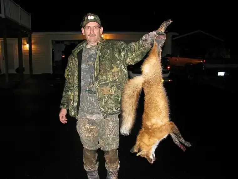 Man in camouflage holding a hanging fox at night in a driveway