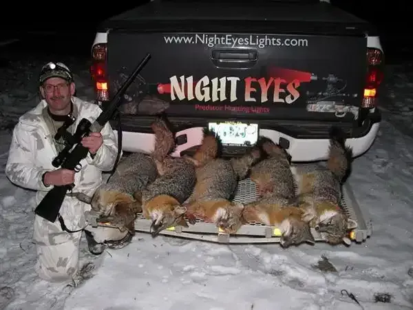 Hunter posing with five ducks beside a black Night Eyes truck in a snowy field at night