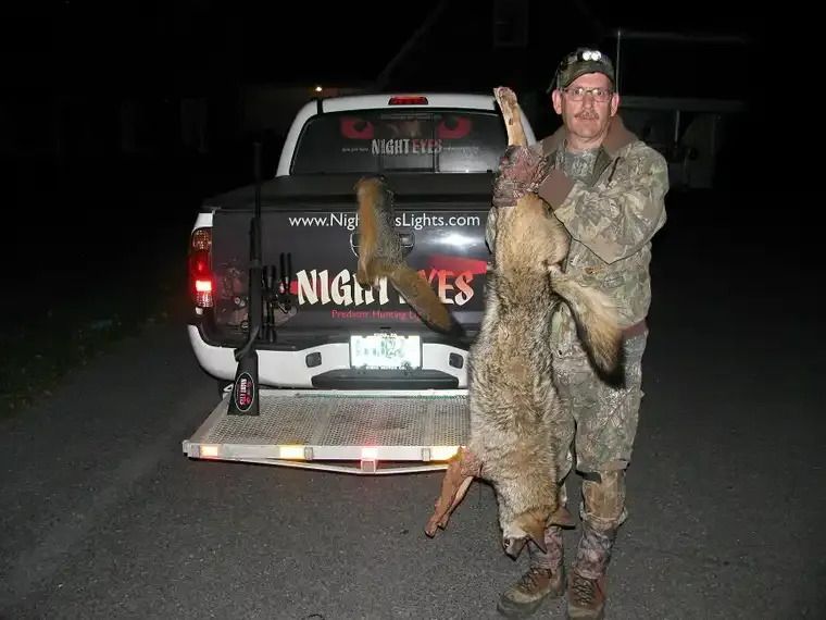 Man posing with a large fish beside a pickup truck at night on a trailer