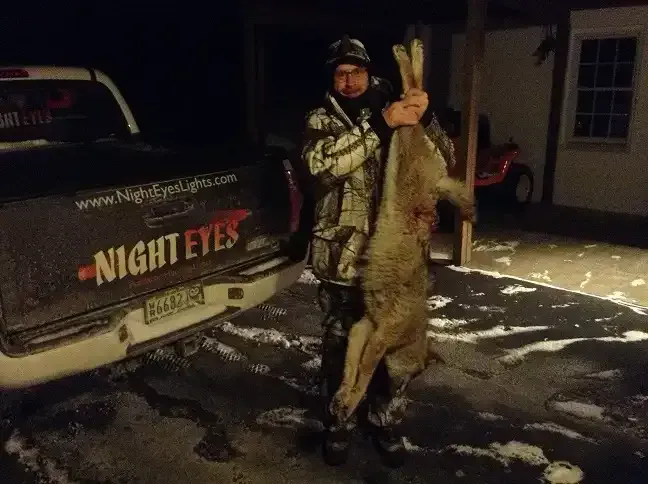 Person holding a large fish beside a truck at night on a snowy driveway
