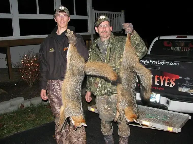 Two men outdoors at night holding large dead fish beside a pickup truck.