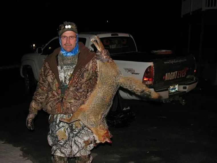 Hunter in camouflage holding a deer beside a pickup truck at night