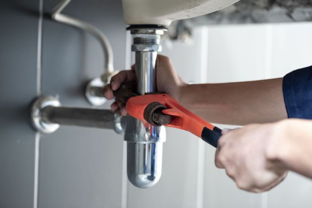 Person using an orange wrench to tighten a chrome sink drain pipe under a bathroom sink